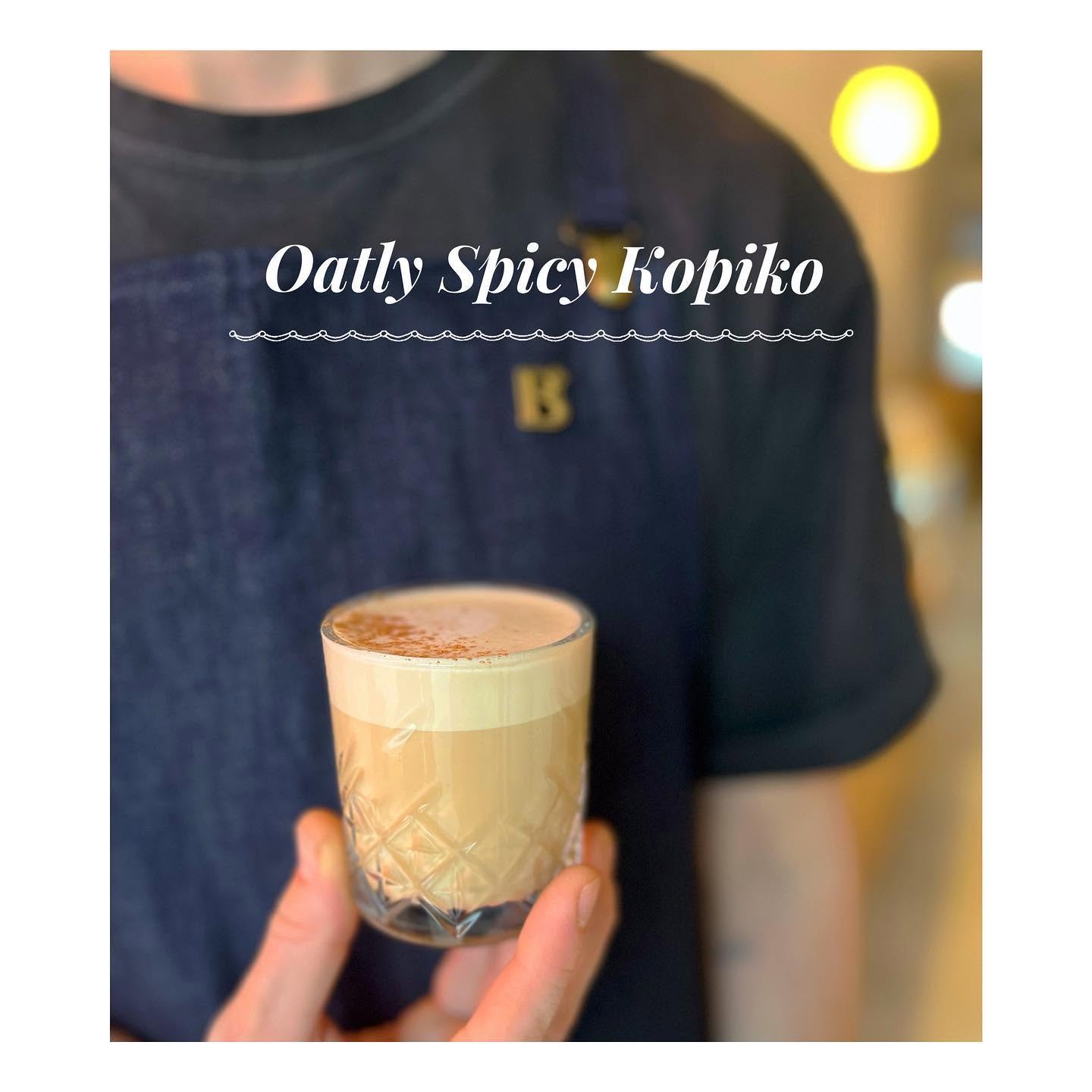 Oatly Spicy Kopiko podawane przez baristę w fartuchu Błysk