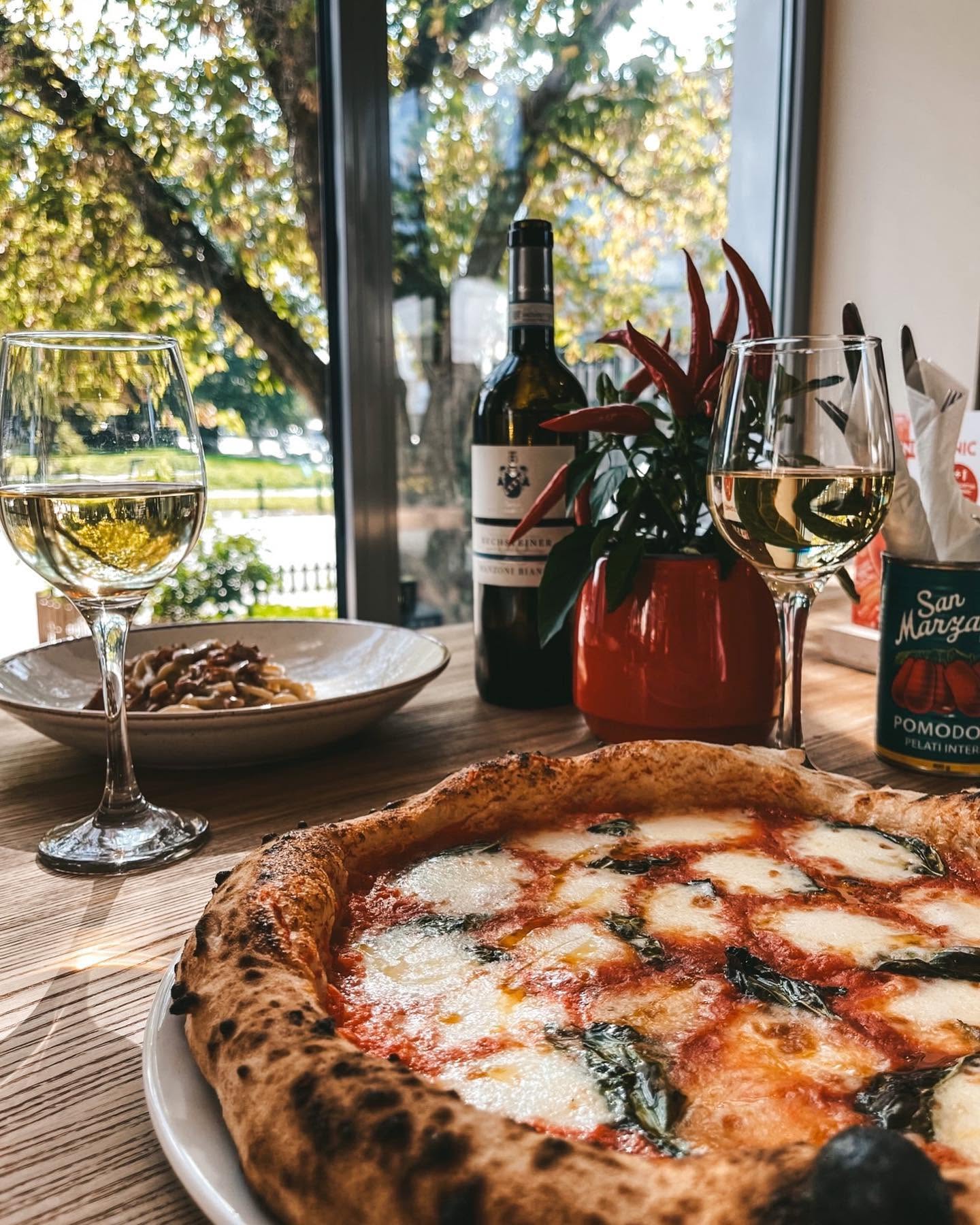 Pizza margherita prosto z pieca, w tle kieliszki wina i okno z widokiem na zieleń